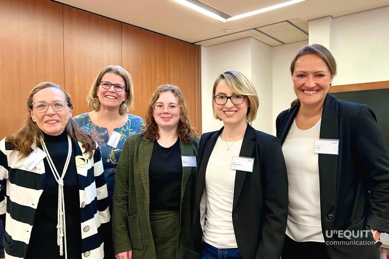 Vor dem hintergrund eines Konferenzraums stehen die Mitglieder von Unequity nebeneinander und lächeln in die Kamera