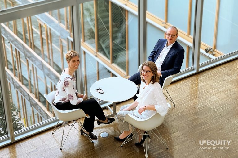 Jutta Rumpf, Simone Schmitt-Schillig und Christian Thomas sitzen im Halbkreis um einen kleinen runden Tisch, vor einer Glaswand zu einem der neun Gärten des Lufthansa Aviation Centers.